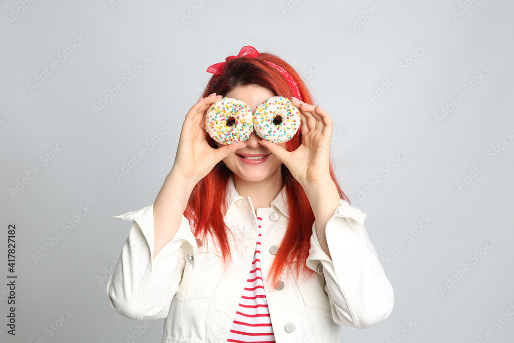 Young woman with bright dyed hair holding donuts near eyes on grey background Young woman with bright dyed hair holding donuts near eyes on grey background