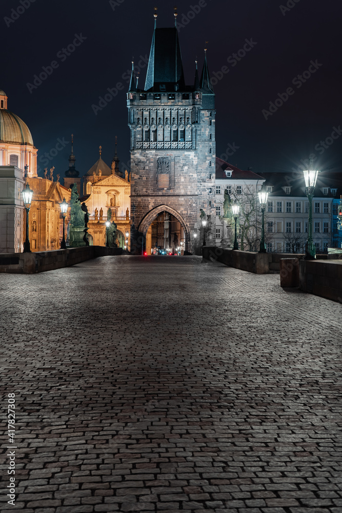 paving and stone tower on Charles Bridge on Vltava river at night in the center of Prague