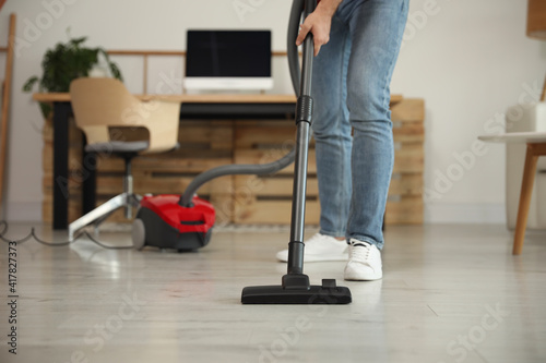 Young man using vacuum cleaner at home, closeup