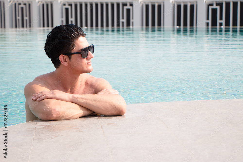 portarit handsome, muscular caucasian white man wearing sunglasses in a swimming pool summer vacation