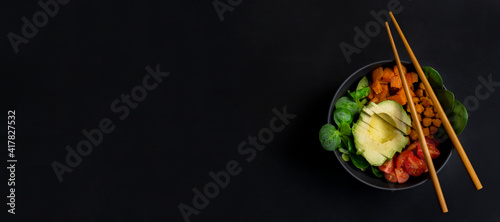 Vegan avocado poke bowl with cherry tomatoes ,spinach and chickpeas.Top view of buddha bowl .Healthy food concept on dark background with copy space.