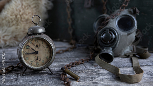 Vintage clock resting on wooden surface with military gas mask and rusty chains in background