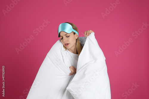 Young woman in sleeping mask wrapped with soft blanket on pink background