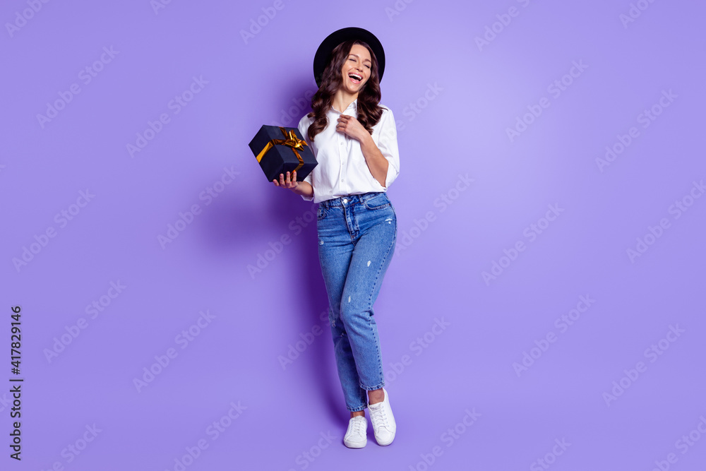 Photo of lovely lady hold box laugh hand chest wear hat white shirt jeans footwear isolated purple color background Photo of lovely lady hold box laugh hand chest wear hat white shirt jeans footwear isolated purple color background