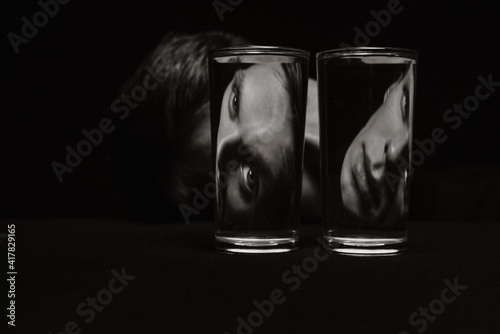 black and white strange portrait of a man looking through two glasses of water photo