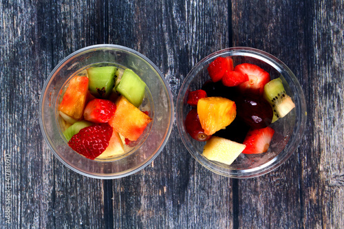 Fototapeta Naklejka Na Ścianę i Meble -  Top view of fresh sliced fruits in plastic cups on wooden background