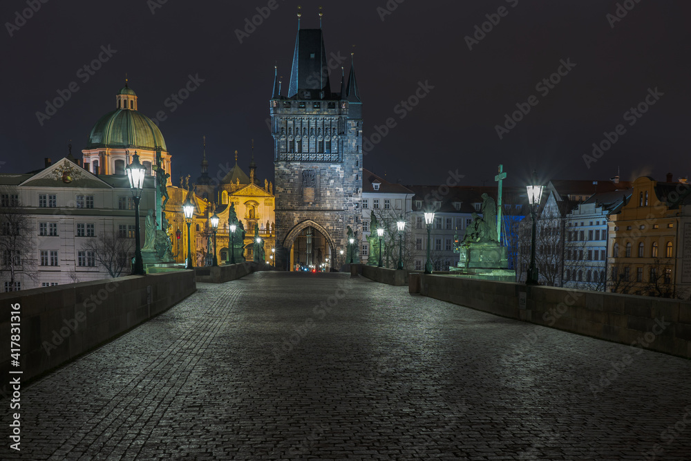 sidewalk with cobblestones and a tower on Charles Bridge and lanterns lit on it at night in the center of Prague