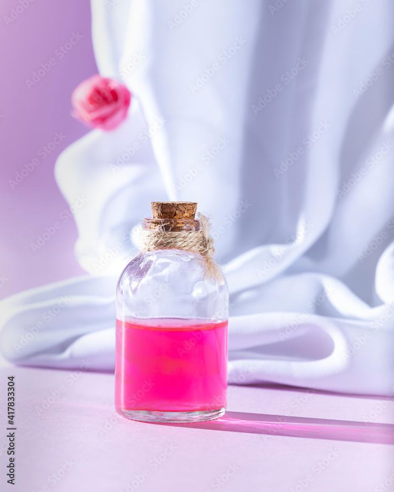 Bottle essential oil or rose water with draped white silk fabric. Spa and aromatherapy cosmetic concept. Bottle essential oil or rose water with draped white silk fabric. Spa and aromatherapy cosmetic concept.