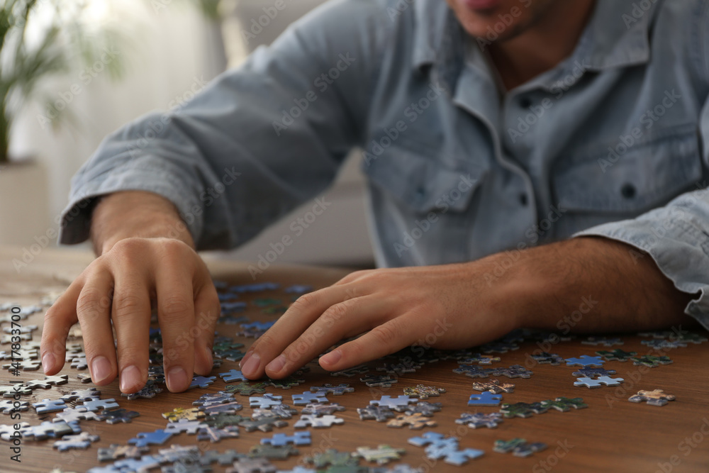 Man playing with puzzles at wooden table indoors, closeup Man playing with puzzles at wooden table indoors, closeup