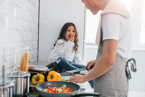 Single father with his daughter is at home together at daytime. Preparing food