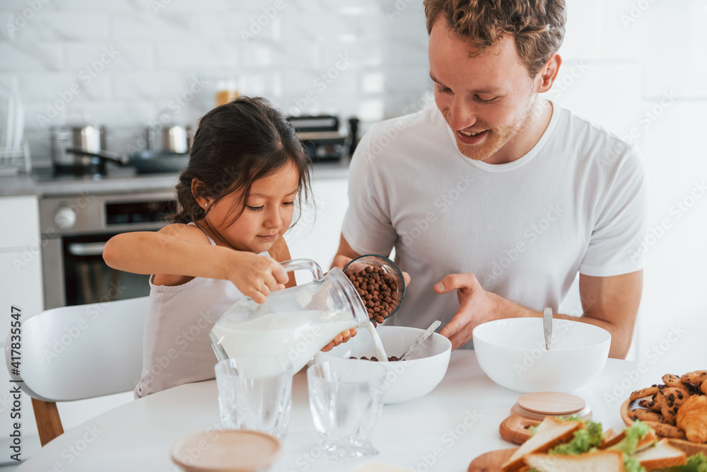 Single father with his daughter is at home together at daytime. Preparing morning food
