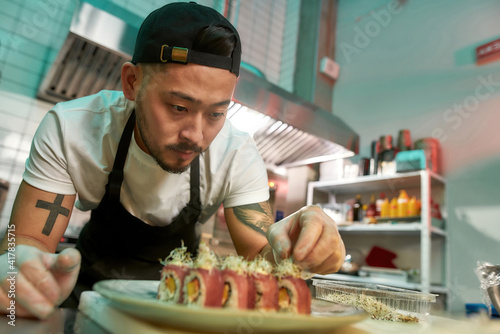 Canvas Print Portrait of experienced sushi chef carefully adding final touch with dedication