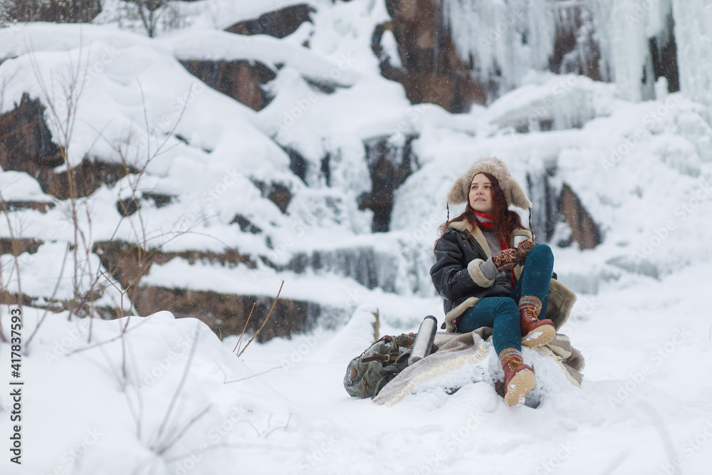 Fototapeta premium Winter outdoor recreation. Young woman drinks hot tea from thermos
