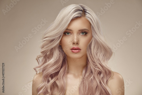 Gorgeous woman with beautiful wavy pink hair on a beige background