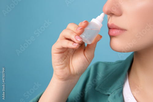 Woman using nasal spray on light blue background, closeup