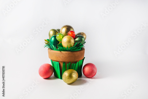 Fototapeta Naklejka Na Ścianę i Meble -  Easter holiday concept. Pot with colored eggs and sweets on a white background
