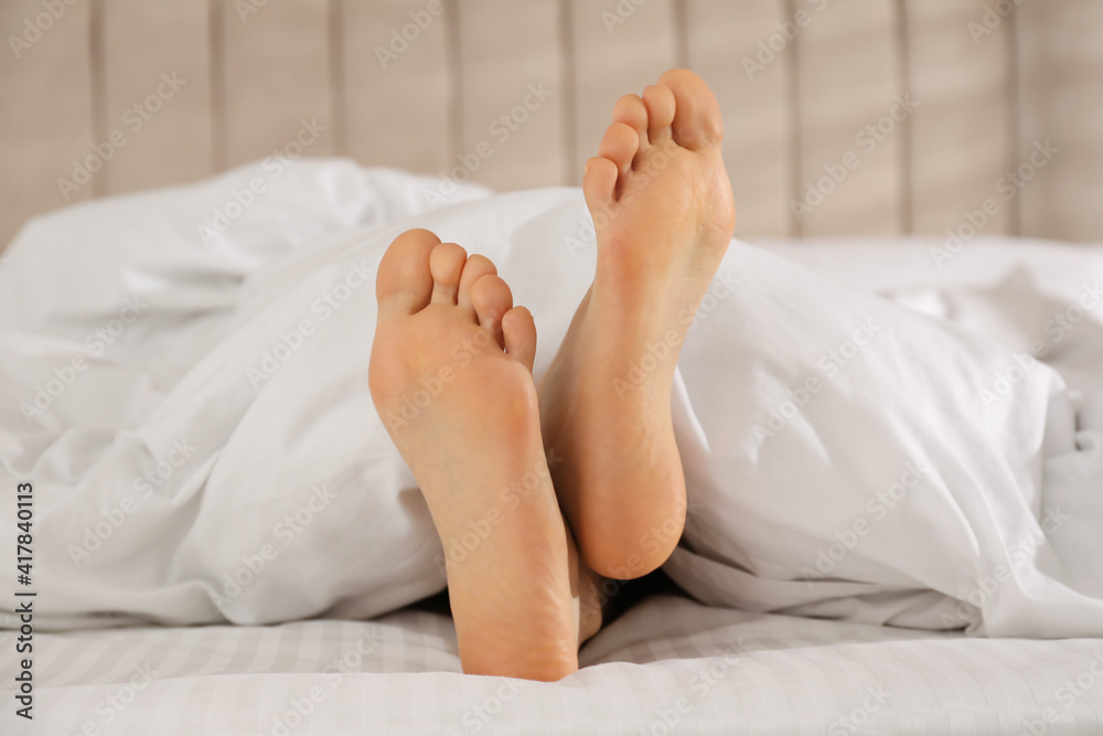 Person in bed with white linens at home, closeup on feet Person in bed with white linens at home, closeup on feet