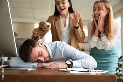 Young women popping paper bag their behind sleeping colleague in office. Funny joke photo