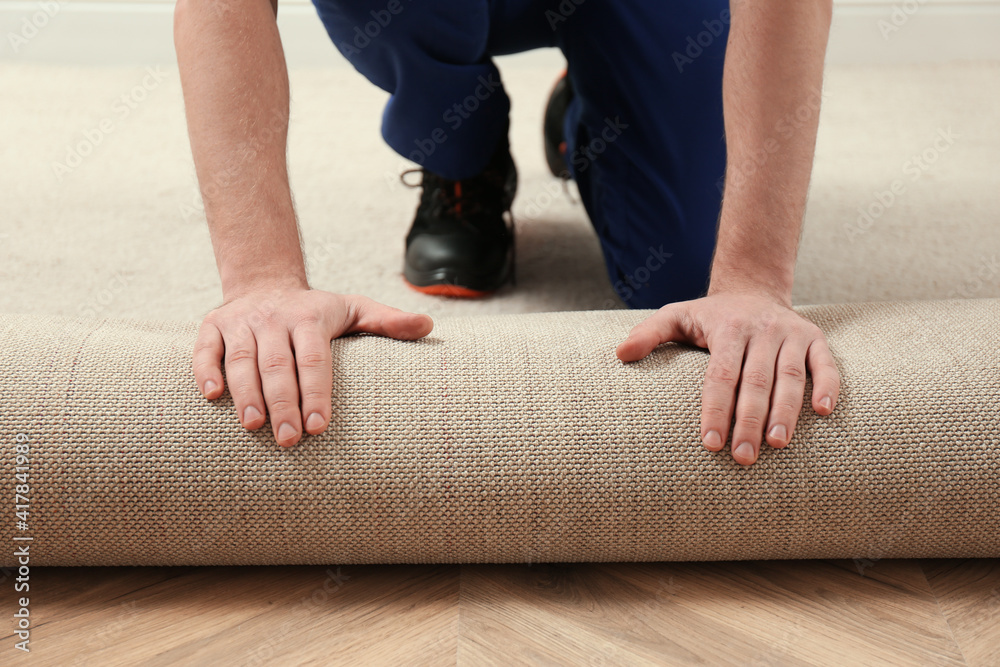 Worker rolling out new carpet flooring indoors, closeup - obrazy, fototapety, plakaty 