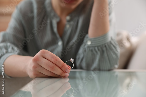 Woman holding wedding ring at table indoors, closeup. Divorce concept