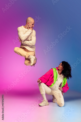 Team. Stylish sportive caucasian couple dancing hip-hop on colorful gradient background at dance hall in neon light. Youth culture, movement, style and fashion, action. Fashionable bright portrait.