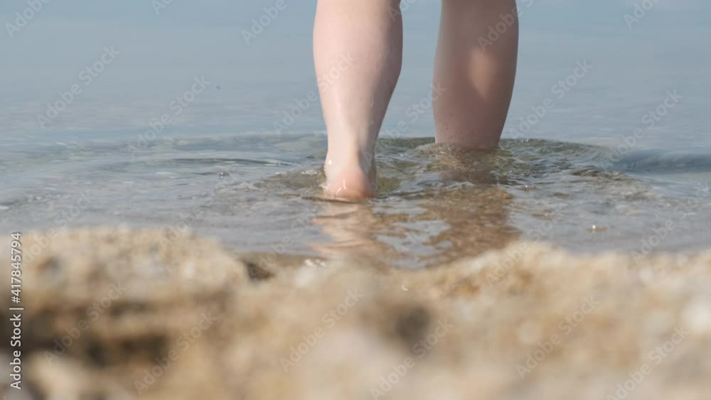 Close-up of feet on the sandy beach, going into the water. Girl goes for a swim. Back view Close-up of feet on the sandy beach, going into the water. Girl goes for a swim. Back view