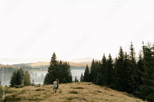 Beautiful young couple in dark green clothes walk by the hands in the mountains in nature