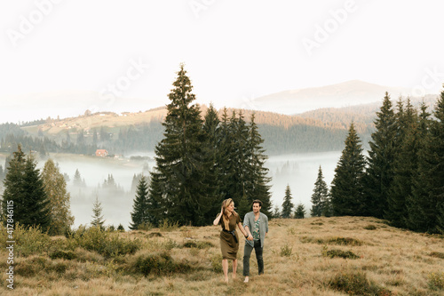 Beautiful young couple in dark green clothes walk by the hands in the mountains in nature © Александр Шуневич