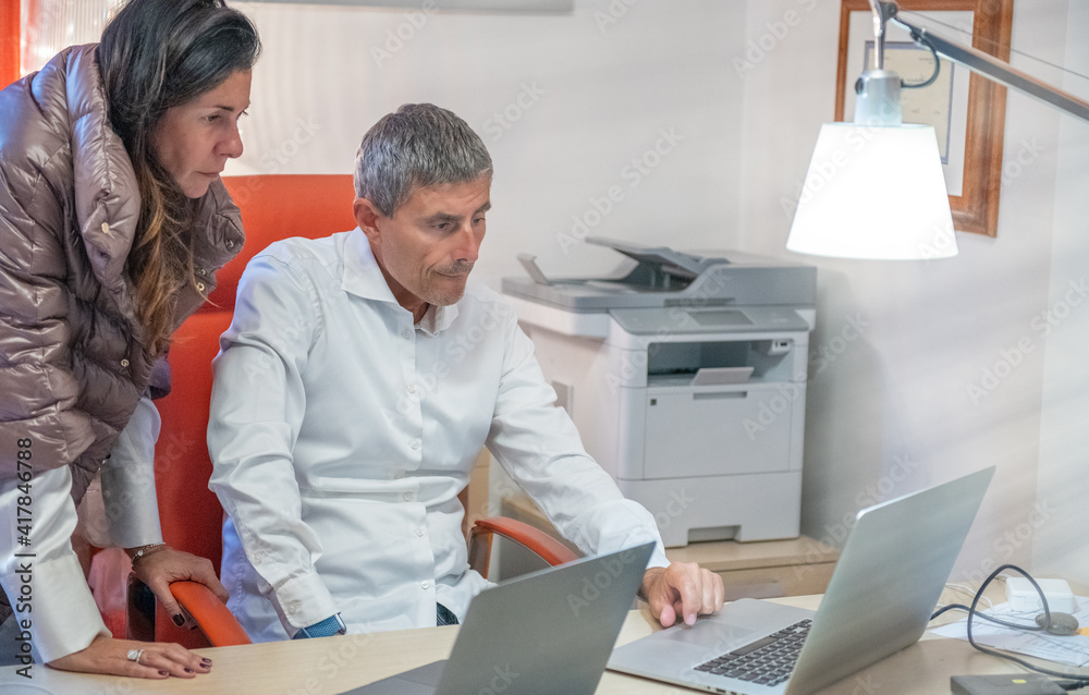 Man and woman near working place with laptop cooperating in office Man and woman near working place with laptop cooperating in office