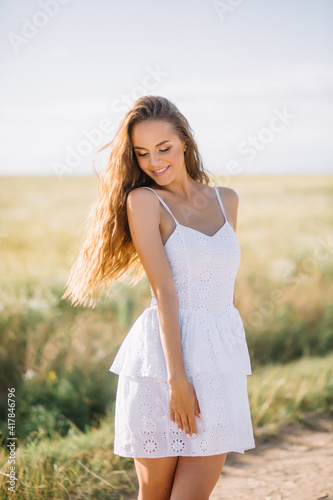 Young woman with long hair in a white dress walks in sunny weather