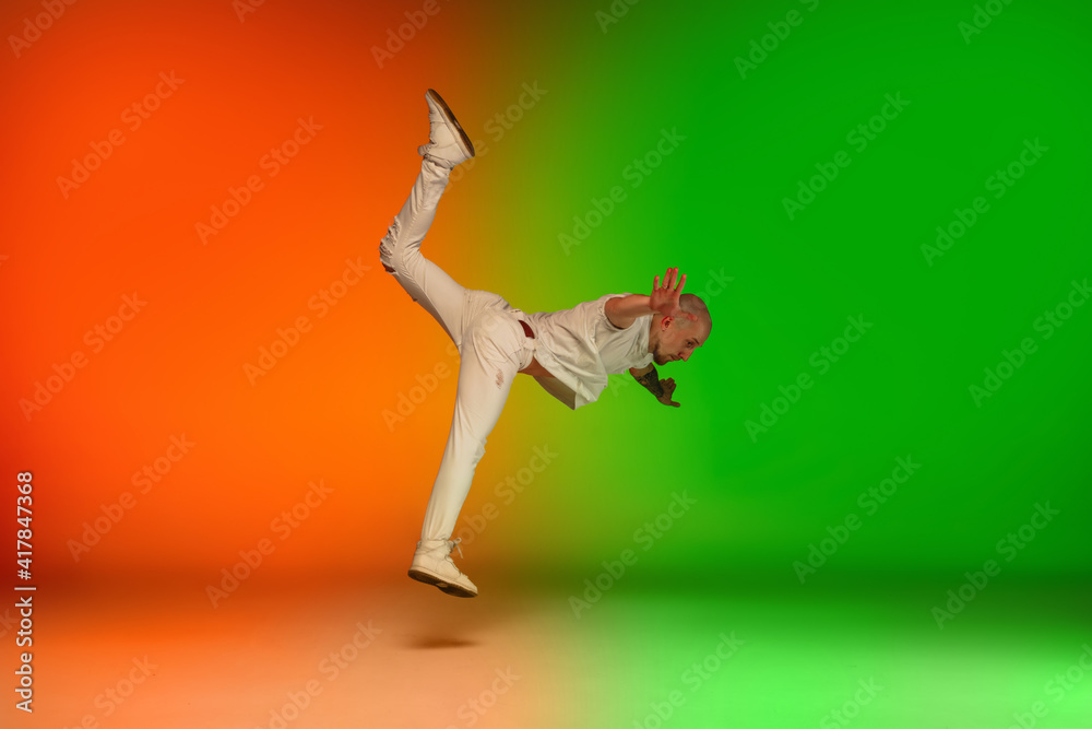 Flying. Stylish sportive caucasian man dancing hip-hop on colorful gradient background at dance hall in neon light. Youth culture, movement, style and fashion, action. Fashionable bright portrait.
