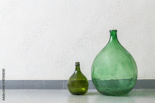 Vintage green glass demijohns used to decor a living room, white wall and grey floor