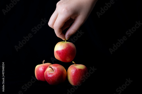A hand is holding a tiny fresh red apple