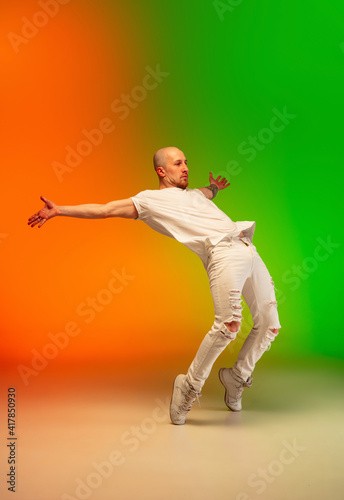 Handsome. Stylish sportive caucasian man dancing hip-hop on colorful gradient background at dance hall in neon light. Youth culture, movement, style and fashion, action. Fashionable bright portrait.