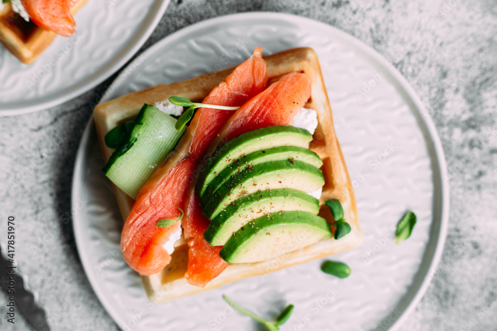 Belgian waffles with salmon, avocado and cream cheese on a white plate. Healthy breakfast at the table Belgian waffles with salmon, avocado and cream cheese on a white plate. Healthy breakfast at the table