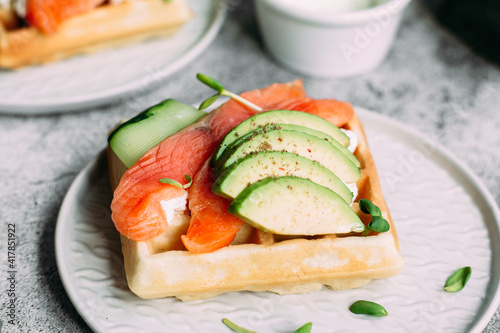 Belgian waffles with salmon, avocado and cream cheese on a white plate. Healthy breakfast at the table