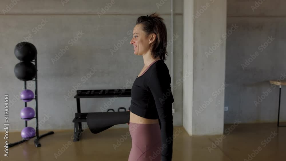 Smiling sporty woman from side view, walking through a gymnasium, arriving to the Yoga center to start the workout. Puts the water bottle and fitness mat on the floor, close up of the feet. Smiling sporty woman from side view, walking through a gymnasium, arriving to the Yoga center to start the workout. Puts the water bottle and fitness mat on the floor, close up of the feet.