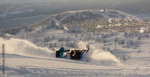 Pro snowmobiler makes a turn and lets a flurry of snow spray from under the caterpillar. sports snowmobile in the mountains. bright skidoo motorbike and suit without brands. Winter fun. panoramic view