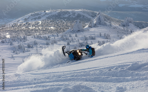 Pro snowmobiler makes a turn and lets a flurry of snow spray from under the caterpillar. sports snowmobile in the mountains. bright skidoo motorbike and suit without brands. Winter fun. panoramic view
