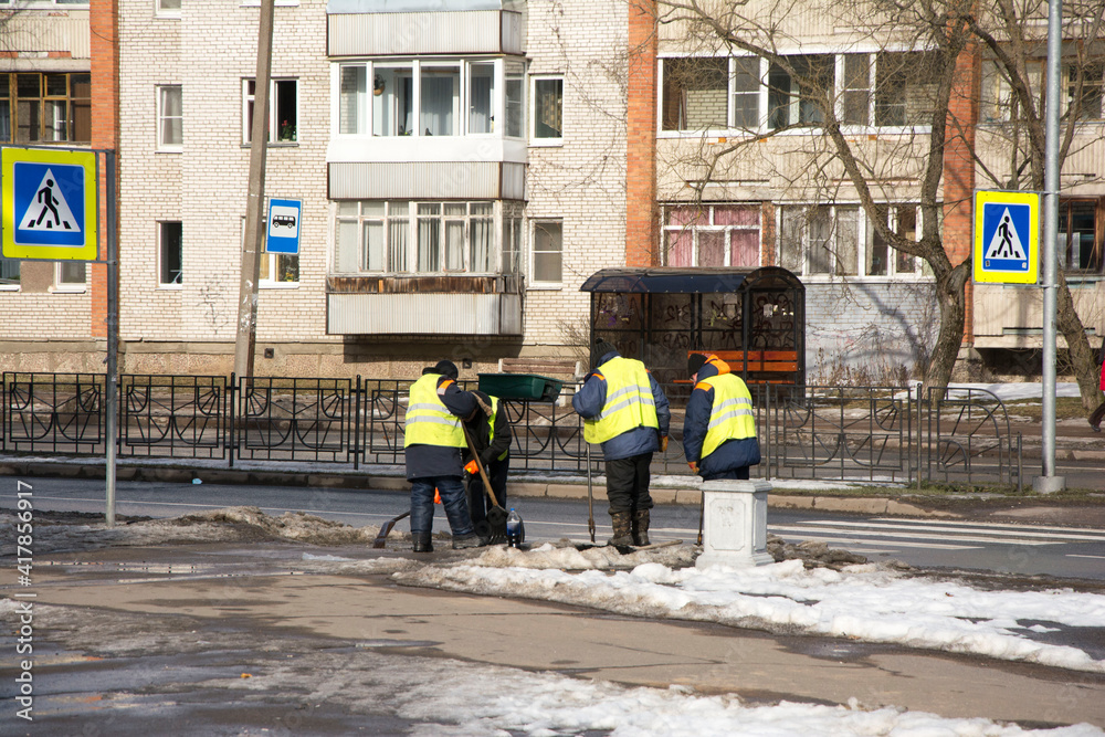Workers in protective vests clean up dirty snow on the street.