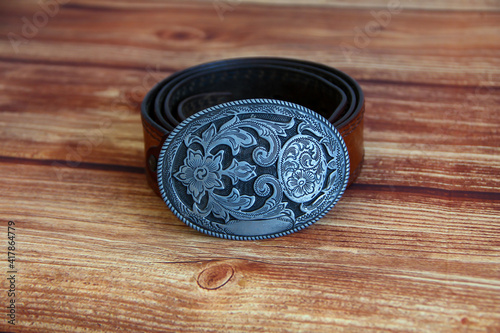 Fotografie Leather cowboy belt with oval patterned buckle on a wooden background