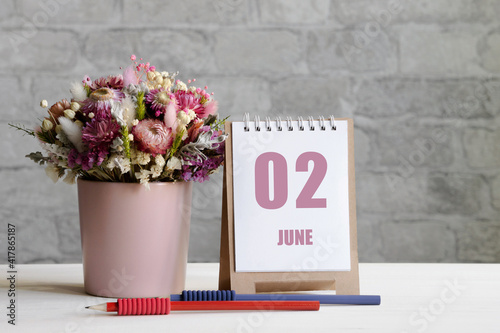 june 02. 02th day of the month, calendar date.A delicate bouquet of flowers in a pink vase, two pencils and a calendar with a date for the day on a wooden surface photo