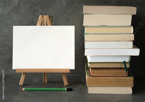 wooden easel with a white board with space for text and books and a pencil on a gray background 