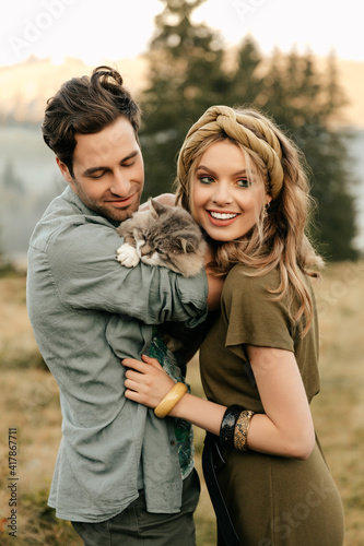 Beautiful sensual couple hug together with the cat and smile cheerfully in nature.
