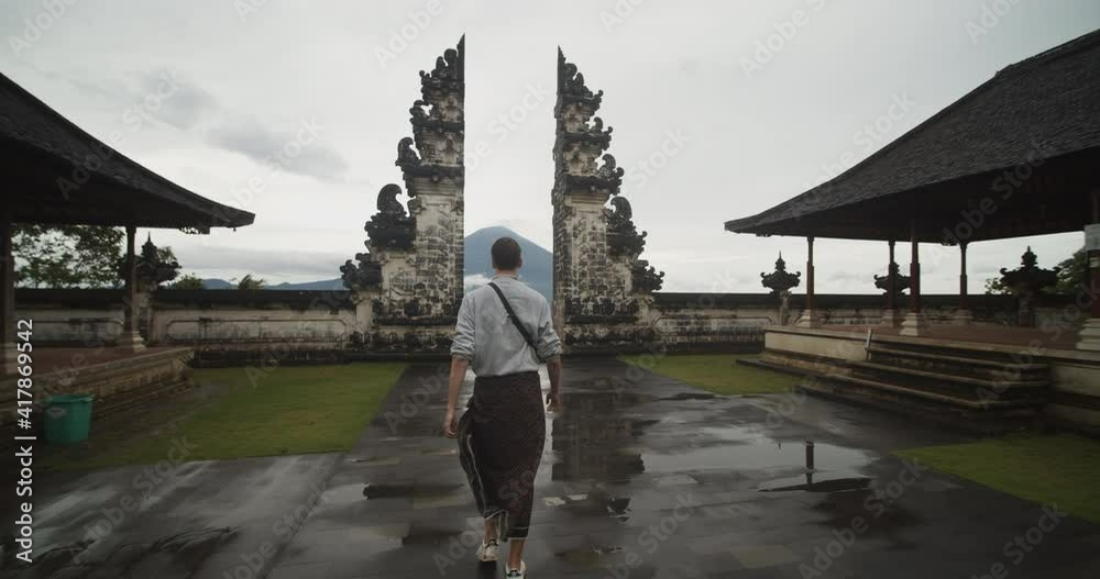 Dolly shot following a white male tourist walking towards a famous black stone pillars in Pura Penataran Agung Lempuyang temple in Bali with Mount Agung volcano in the background