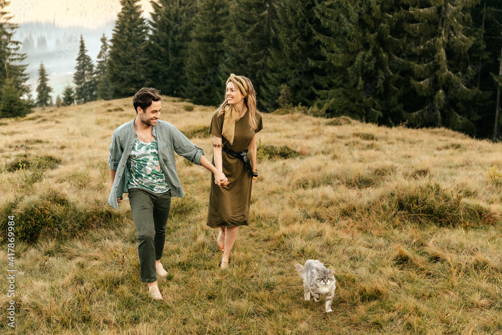 A beautiful couple in love are walking with the cat and smiling cheerfully in nature.