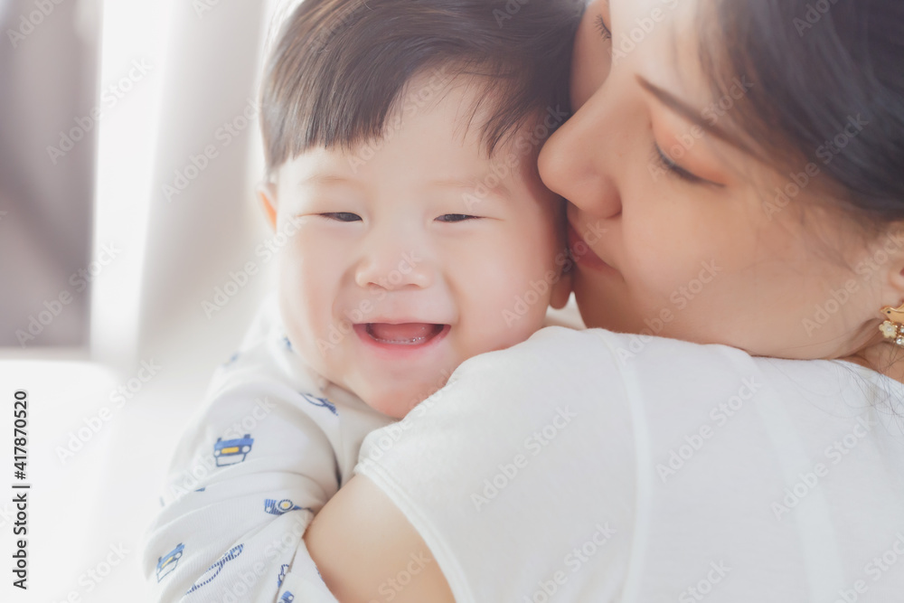 Close up portrait of young beauty Asian mother kissing her newborn baby boy's feet and having fun. Mom playing with her baby. Asia mother's day concept banner Close up portrait of young beauty Asian mother kissing her newborn baby boy's feet and having fun. Mom playing with her baby. Asia mother's day concept banner