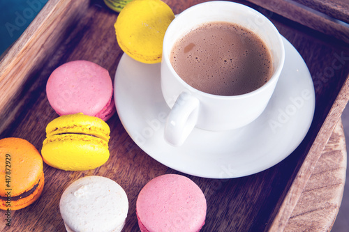 French colored macaroons with white cup of coffee on wooden background