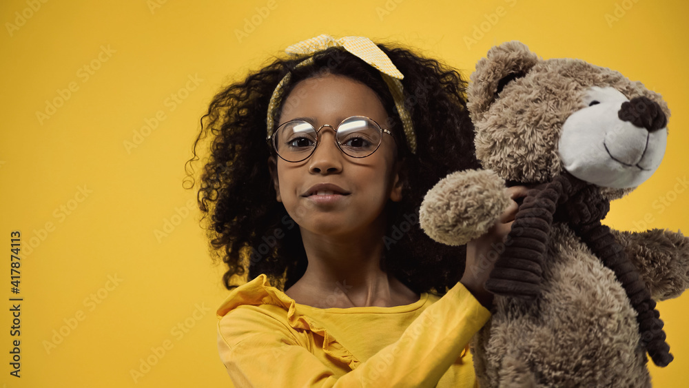 curly african american kid in glasses holding teddy bear isolated on yellow curly african american kid in glasses holding teddy bear isolated on yellow