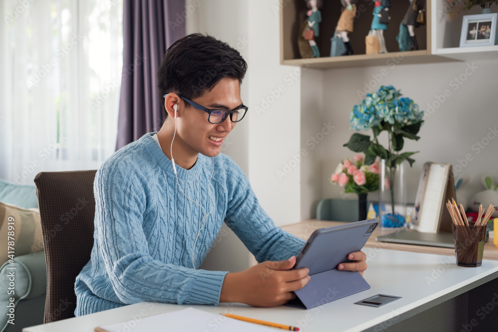 Young Asian man wearing headphones using a tablet at home.